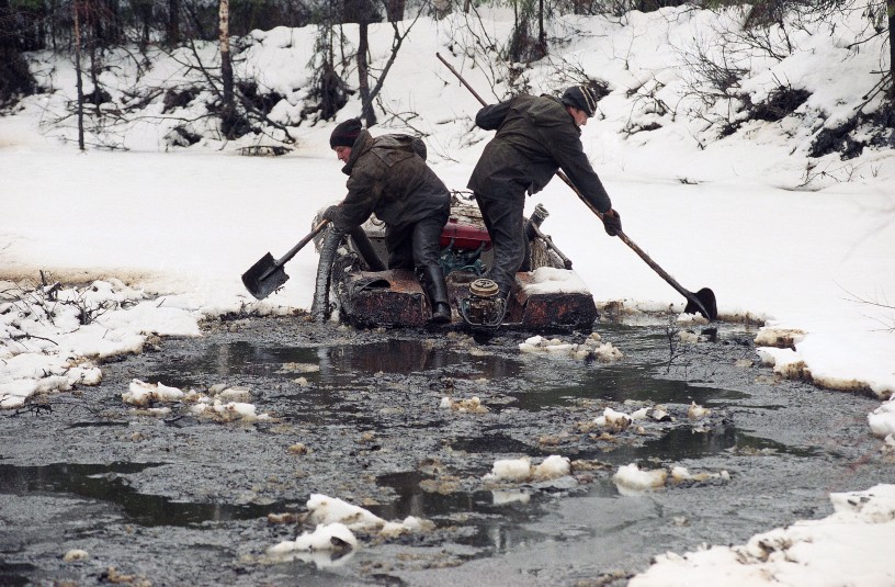 Two Russian oil workers use a boat and shovels to gather oil and mud from the waters of a small river, a tributary of the Kolva River, some 37 miles north of Usinsk, an Arctic town six miles from the Arctic Circle in Russia, Friday, Oct. 28, 1994. 